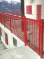AluminiumZaun und Tür Circle in Sonderfarbton rot, als Geländer einer Terrasse mit Bergpanorama verbaut, Kundenfoto