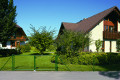 Gartenzaun mit Wellengittertor und Maschendrahtzaun in einbetonierter Variante vor Haus mit Garten und Wiese